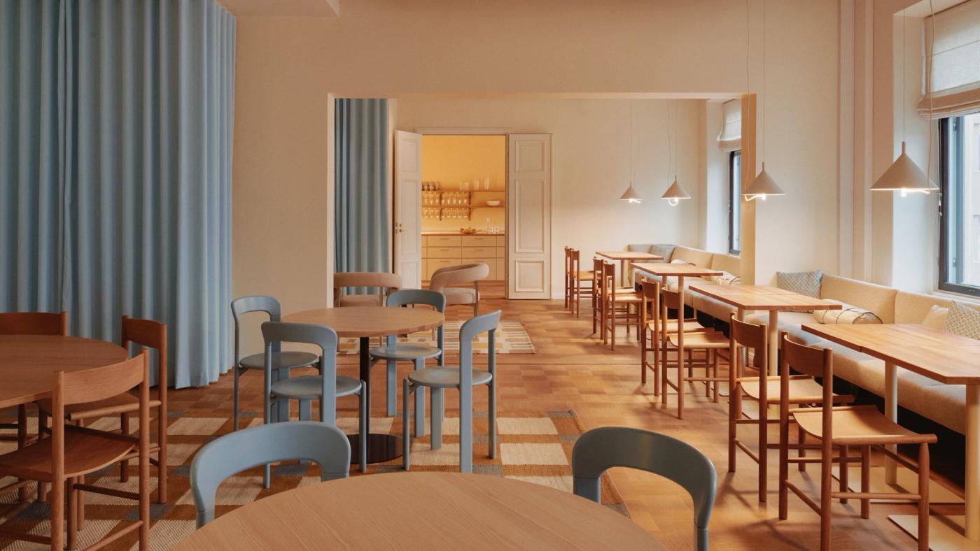 Avara ja valoisa working café -tila, jossa pyöreitä puupöytiä, sinisiä ja tammipuisia tuoleja sekä pitkä pehmustettu penkki ikkunan edessä.