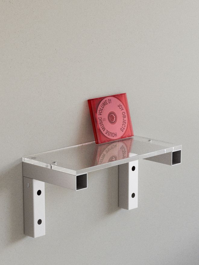 A transparent glass wall shelf with metal brackets holds a red book.