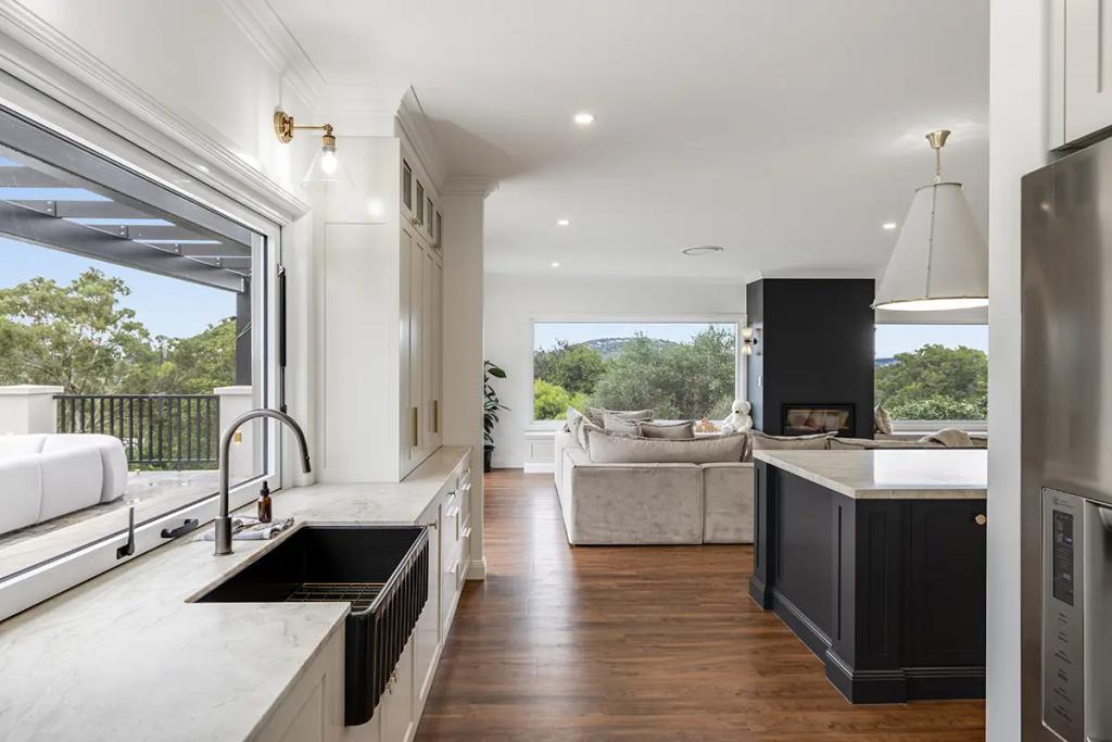 Hodgsonvale House Renovation (A contemporary kitchen with white cabinets, dark island, black sink, and outdoor view.)