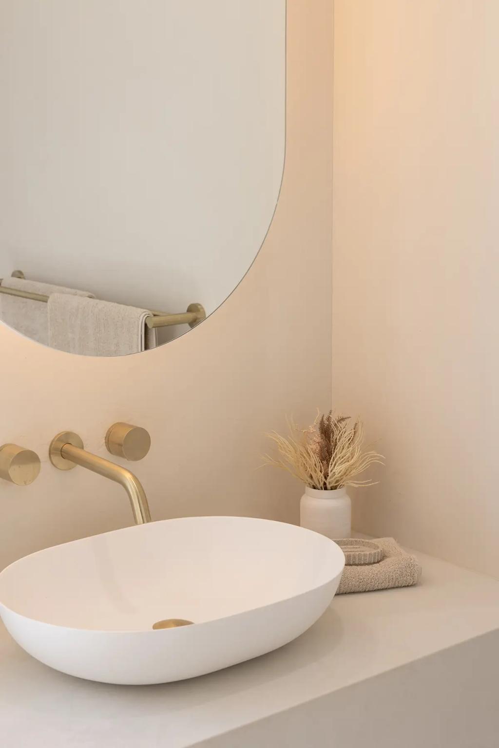 Project Vuse (A modern bathroom with a white oval sink, gold faucet, round mirror, and decorative dried plants in a small white vase)