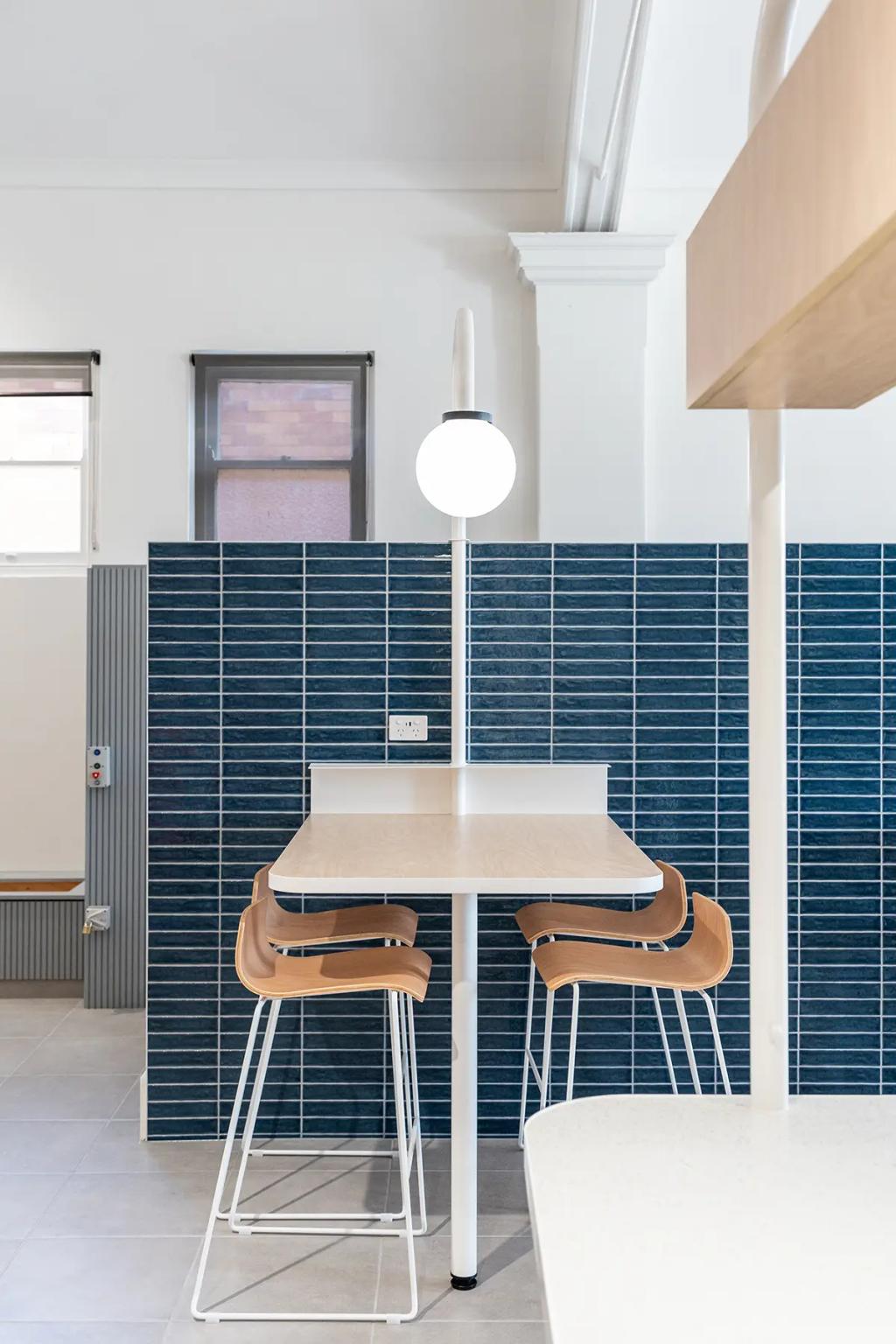 Downlands College Toowoomba Refurbishment (Compact high table with four wooden barstools and built-in globe light, set against dark blue tile wall.)