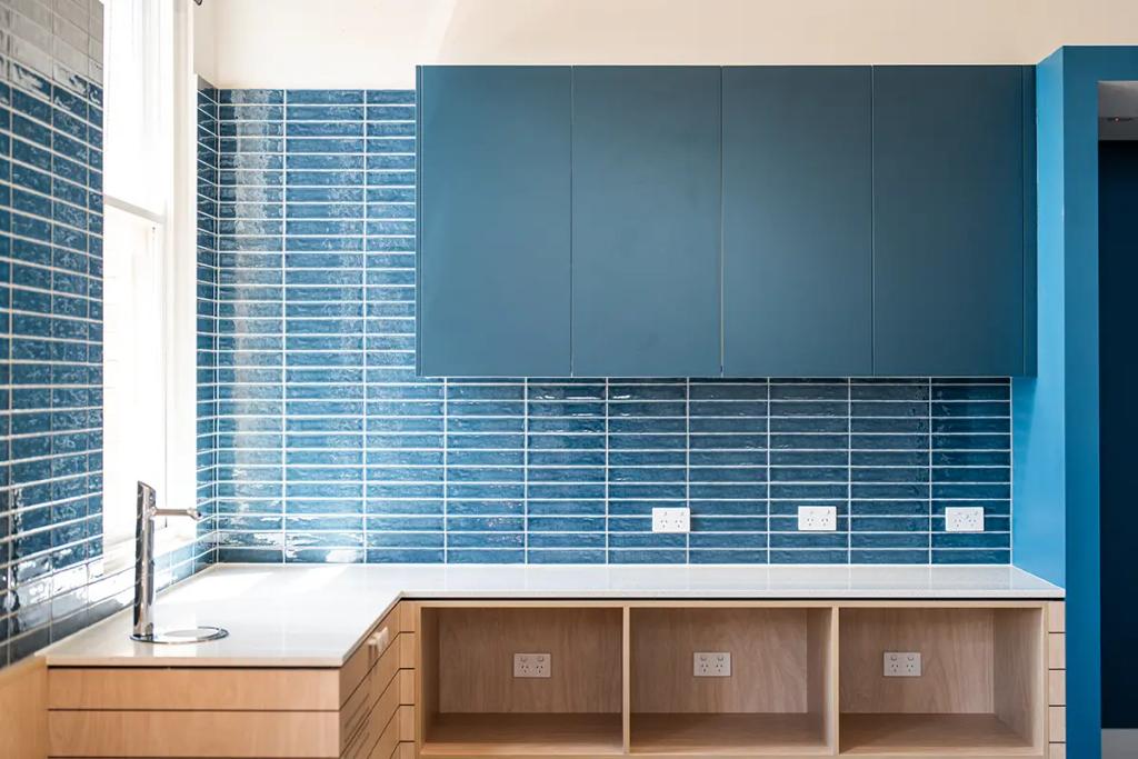 Downlands College Toowoomba Refurbishment (Modern kitchenette with glossy blue tile backsplash, sleek upper cabinets, and open wood shelving below.)
