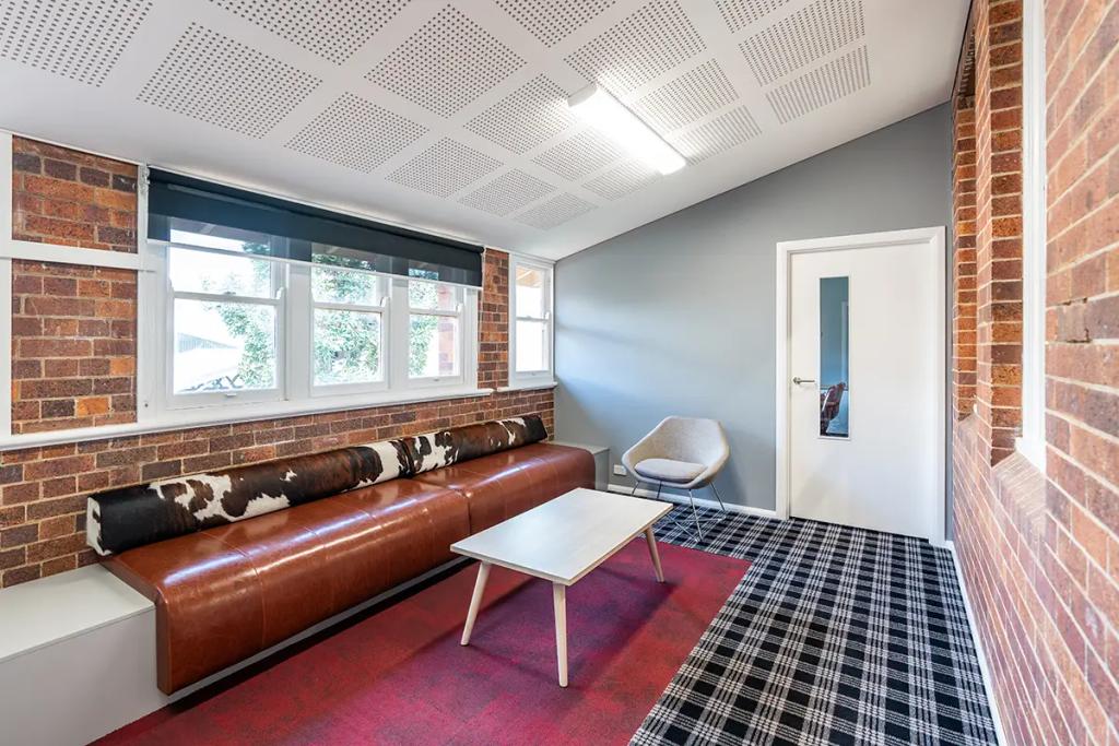 Downlands College Toowoomba Refurbishment (Cozy lounge with a brown leather bench, cowhide bolster, modern coffee table, and gray accent chair.)