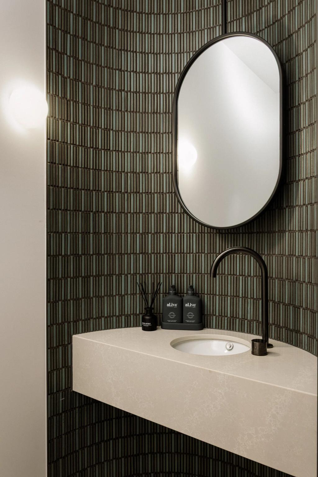Lavish Morada (Modern powder room with curved tiled wall, floating vanity, black faucet, and oval mirror.)