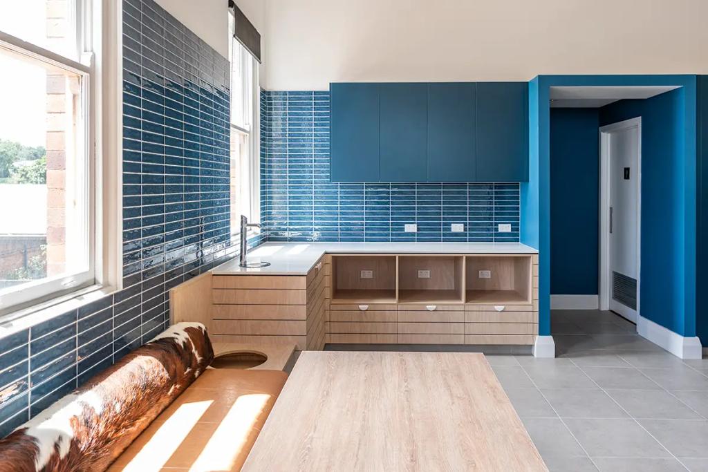 Downlands College Toowoomba Refurbishment (Modern kitchenette with blue tile backsplash, wood cabinetry, and a bench seat beside large windows.)