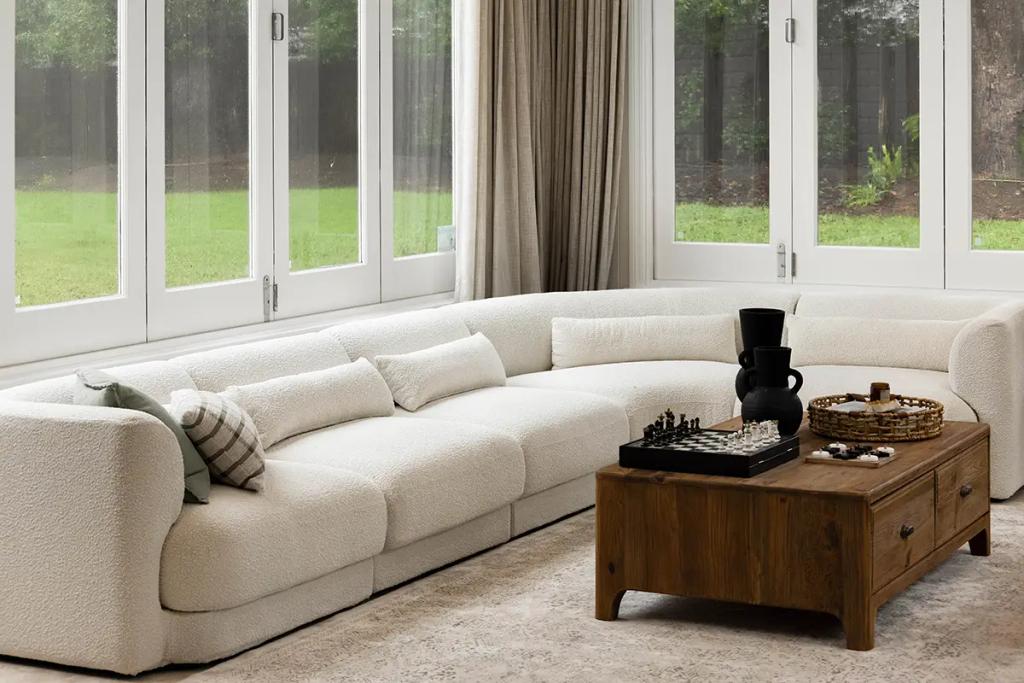 Project Franklin (Curved cream sofa and wood table in sunlit living room.)