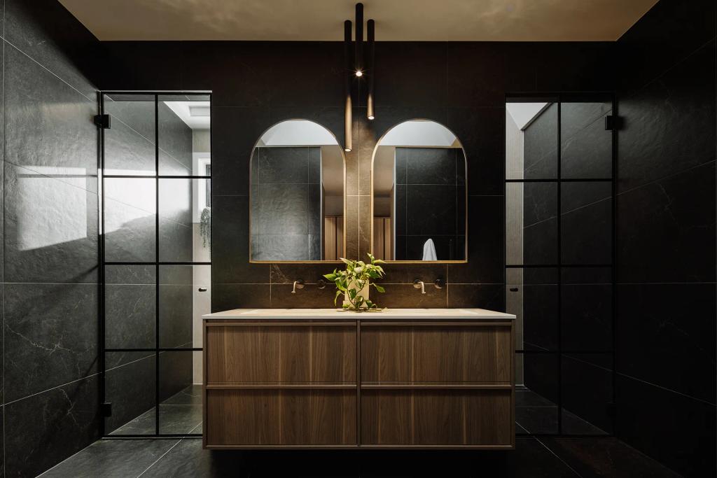 Lavish Morada (Modern bathroom with double wood vanity, arched mirrors, black tile walls, and pendant lights.)