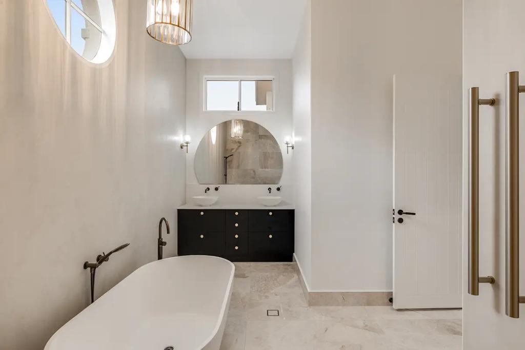 Hodgsonvale House Renovation (A minimalist bathroom with a freestanding tub, dark vanity, and dual round mirrors.)