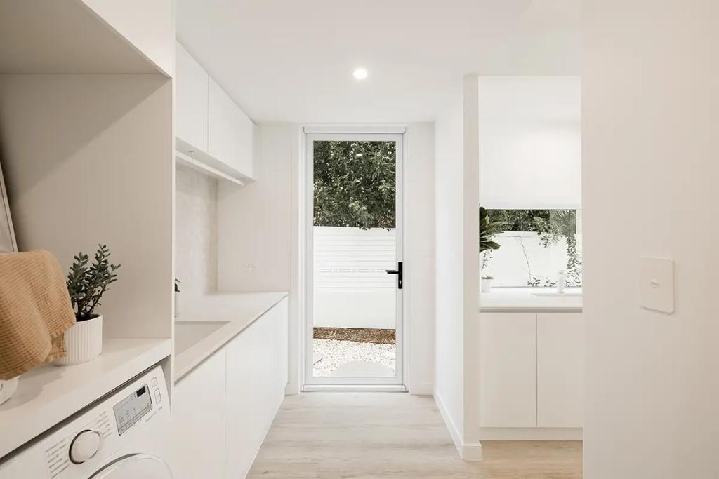 Modern minimalist laundry room with white cabinets, washing machine, and a glass door leading to the outside