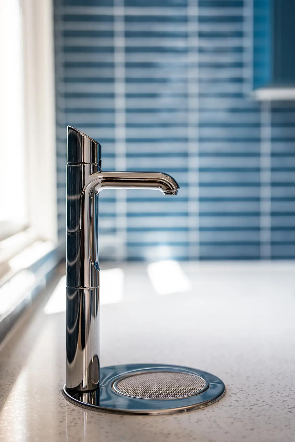 Downlands College Toowoomba Refurbishment (Close-up of a modern chrome tap on a speckled countertop, with glossy blue tile backsplash in background.)