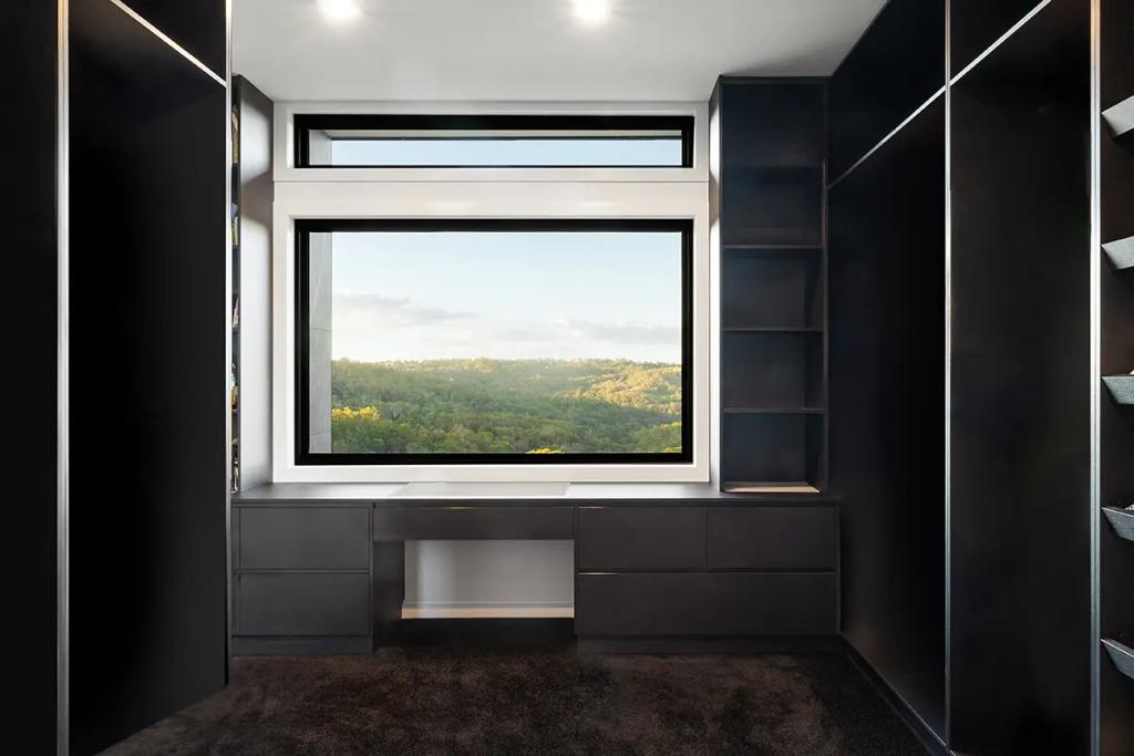 Modern closet design with built-in drawers and shelves framing a large window with a view of a green forest landscape