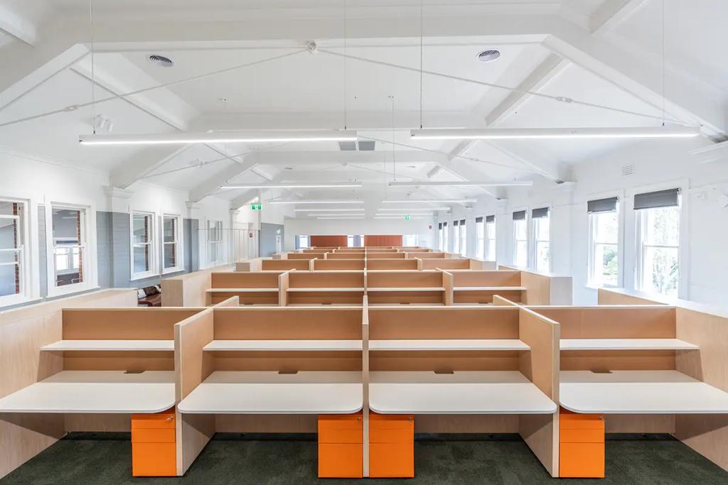 Downlands College Toowoomba Refurbishment (Bright open-plan office with rows of light wood workstations, white desks, and orange drawer units.)