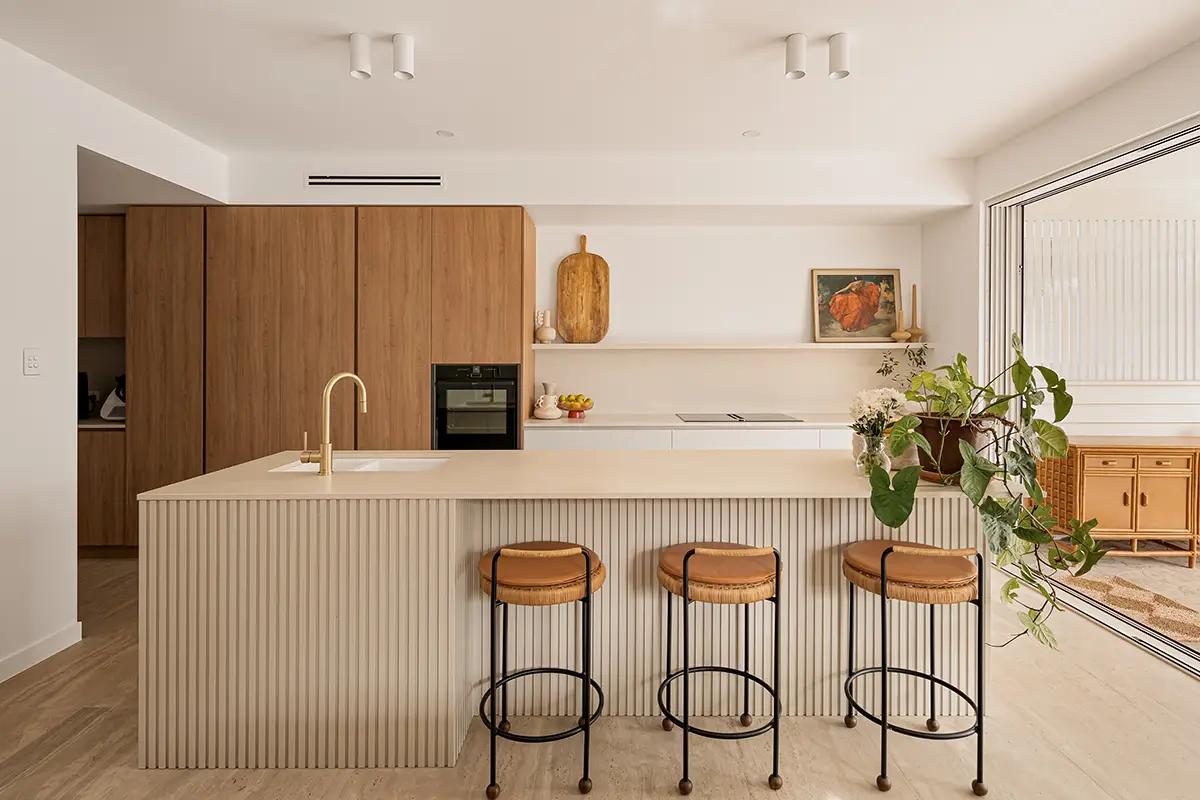 Project Alice (Fluted cream island with rattan stools, timber cabinetry and gold gooseneck tap)