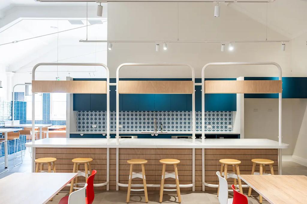 Downlands College Toowoomba Refurbishment (Contemporary communal kitchen with patterned backsplash, wood-accented island, and wooden bar stools.)