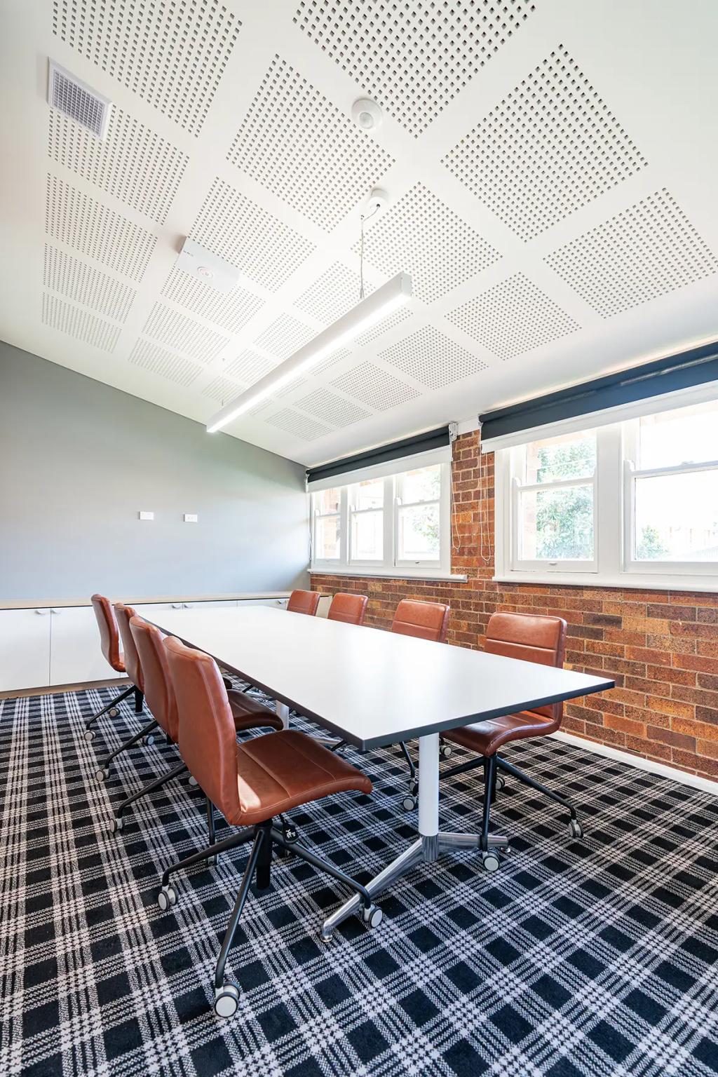 Downlands College Toowoomba Refurbishment (Modern meeting room with a long white table, brown leather chairs, plaid carpet, and brick walls.)