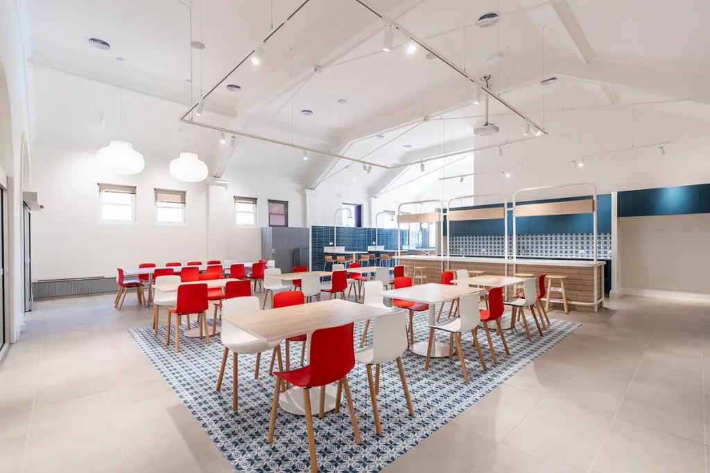 Downlands College Toowoomba Refurbishment (Spacious dining area with wooden tables, red and white chairs, patterned blue floor tiles, and open kitchenette.)