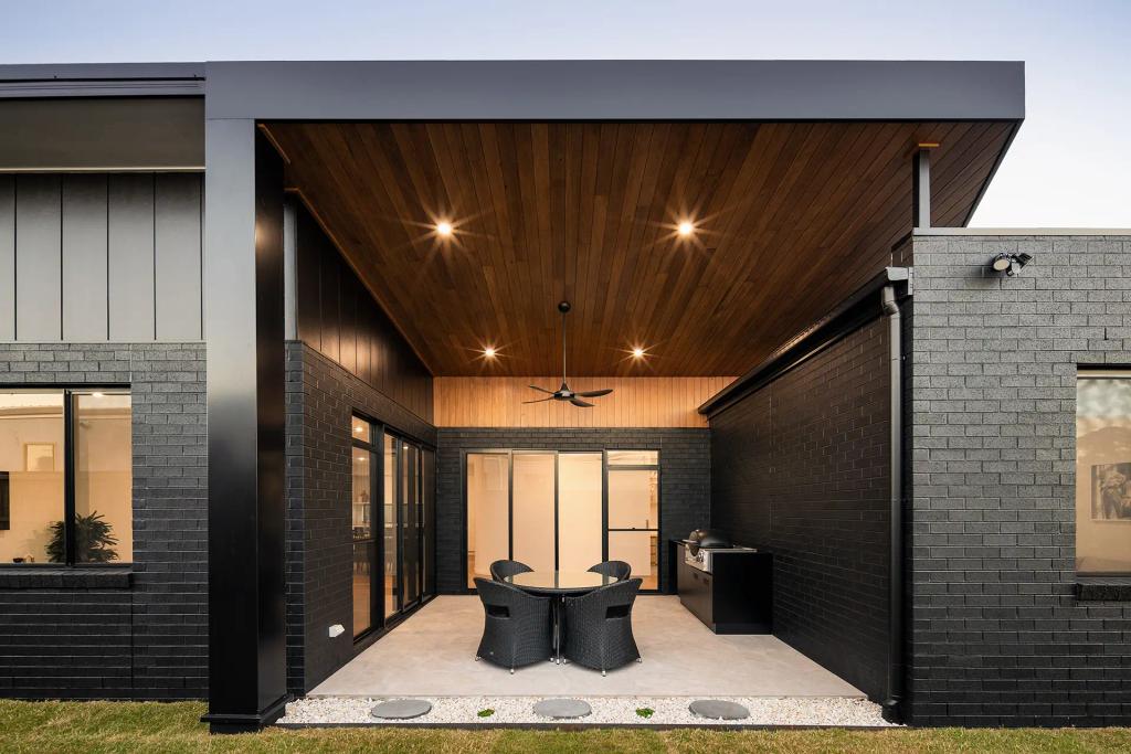 Project Ward (A modern outdoor patio with black brick walls, wooden ceiling, round table, wicker chairs, and grill)