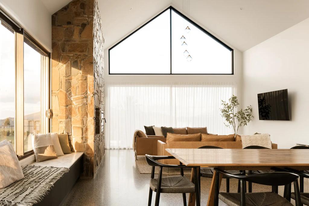 Project Mount Rascal (Living room with stone fireplace, vaulted ceiling, large windows, beige couch, and wooden dining table)