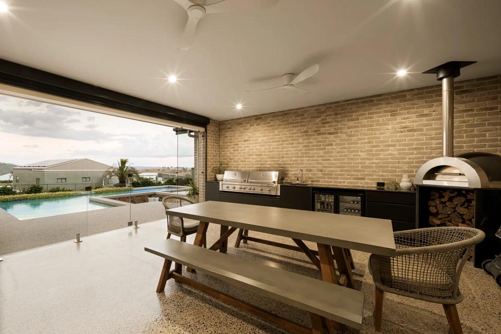 Project Mount Rascal (Outdoor kitchen with brick wall, barbecue grill, wood-fired oven, dining table, and pool view)