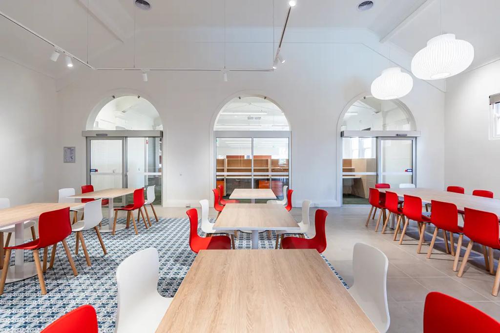 Downlands College Toowoomba Refurbishment (Modern dining area with wood tables, red and white chairs, arched glass doors, and patterned tile flooring.)