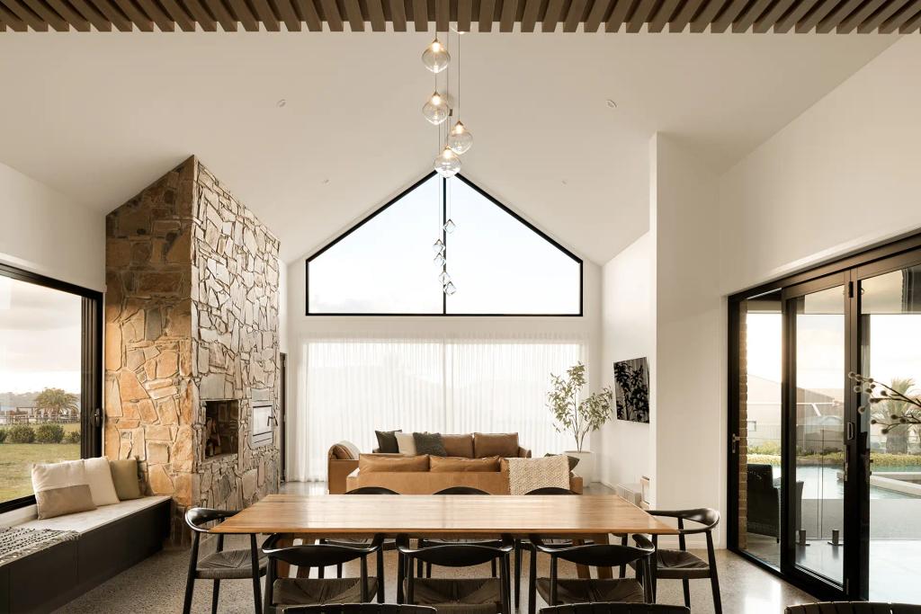 Project Mount Rascal (Modern living room with vaulted ceiling, stone fireplace, large windows, and a dining table with black chairs)