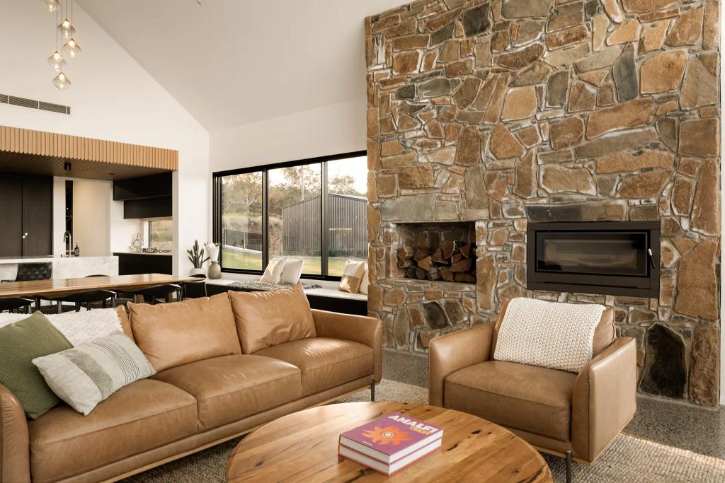 Project Mount Rascal (Cozy living area with stone fireplace, leather sofa, armchair, and large windows overlooking the yard)