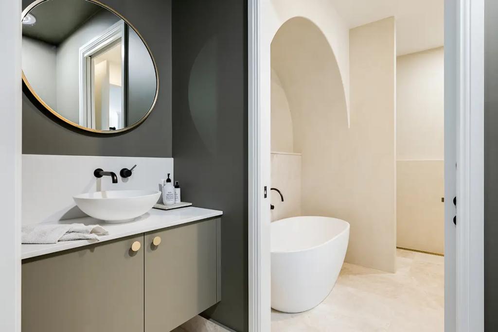 Hodgsonvale House Renovation (A split image showing a modern bathroom vanity and a freestanding tub in an arched alcove.)