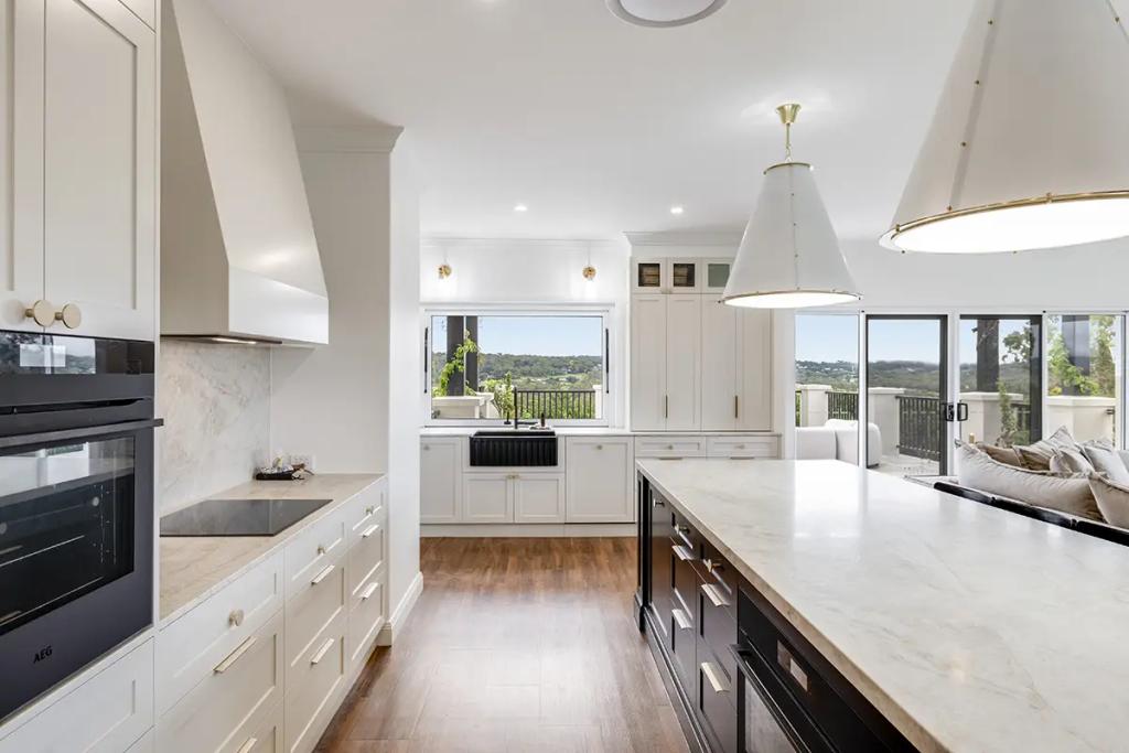 Hodgsonvale House Renovation (A spacious, well-lit kitchen featuring white cabinets, dark island, and marble countertops.)