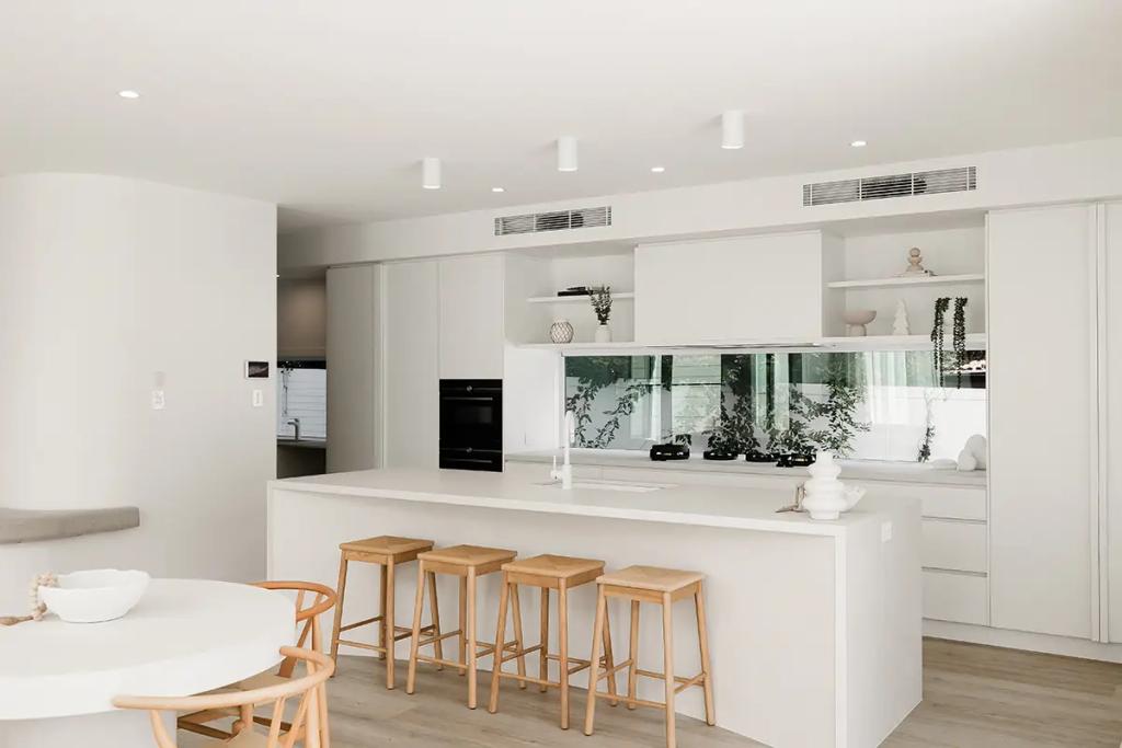 Project Vuse (A modern kitchen with white walls and cabinets, a round dining table with wooden chairs, and a kitchen island with bar stools)