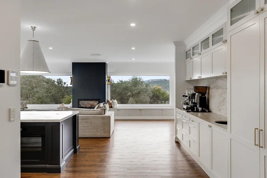 Hodgsonvale House Renovation (A sleek white kitchen with a dark island, hardwood floors, and a living area beyond.)