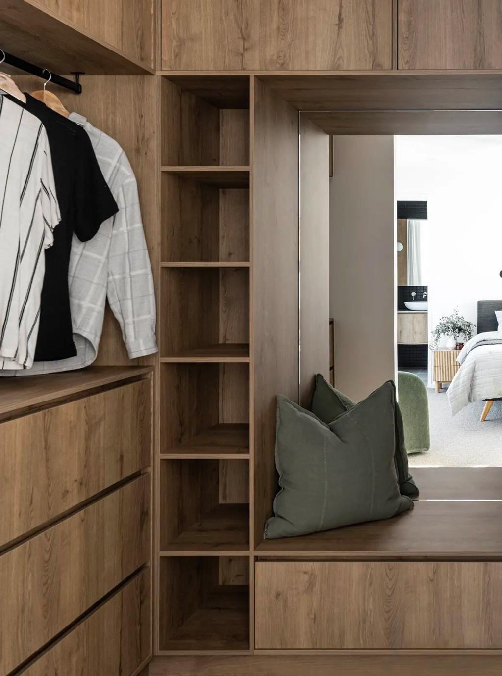 Project Ward 2.0 (A modern walk-in closet with wood cabinetry, hanging clothes, open shelving, and a bench with green cushions)