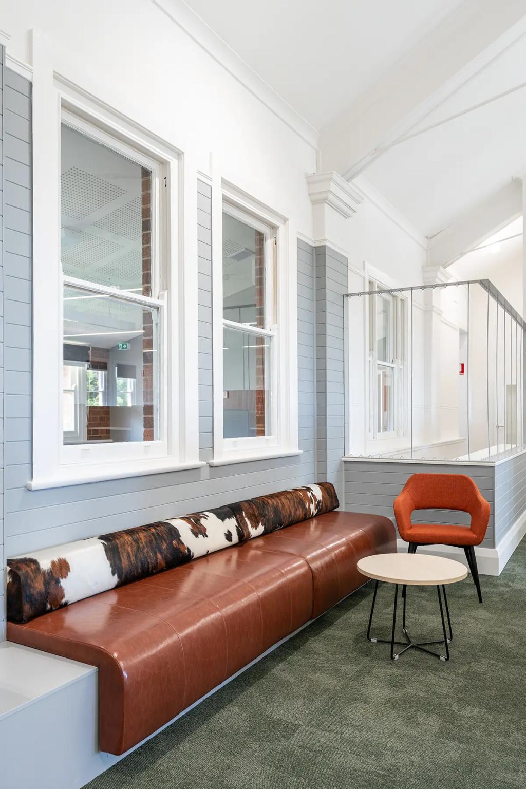 Downlands College Toowoomba Refurbishment (Stylish lounge with a brown leather bench, cowhide bolster, orange accent chair, and round coffee table.)