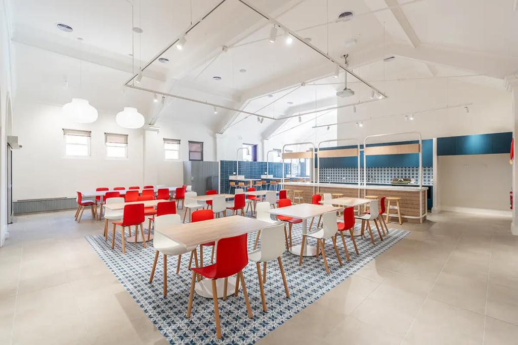 Downlands College Toowoomba Refurbishment (Spacious dining area with red and white chairs, tiled rug design, and modern open kitchen in back.)