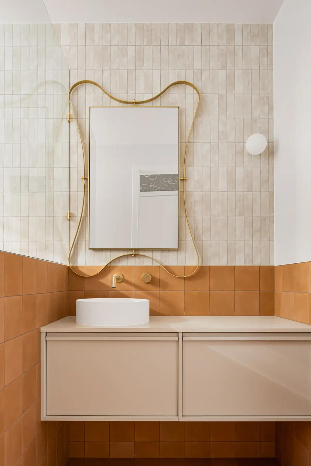 Project Alice (A modern bathroom with a gold-framed mirror, and white and brown tiles)