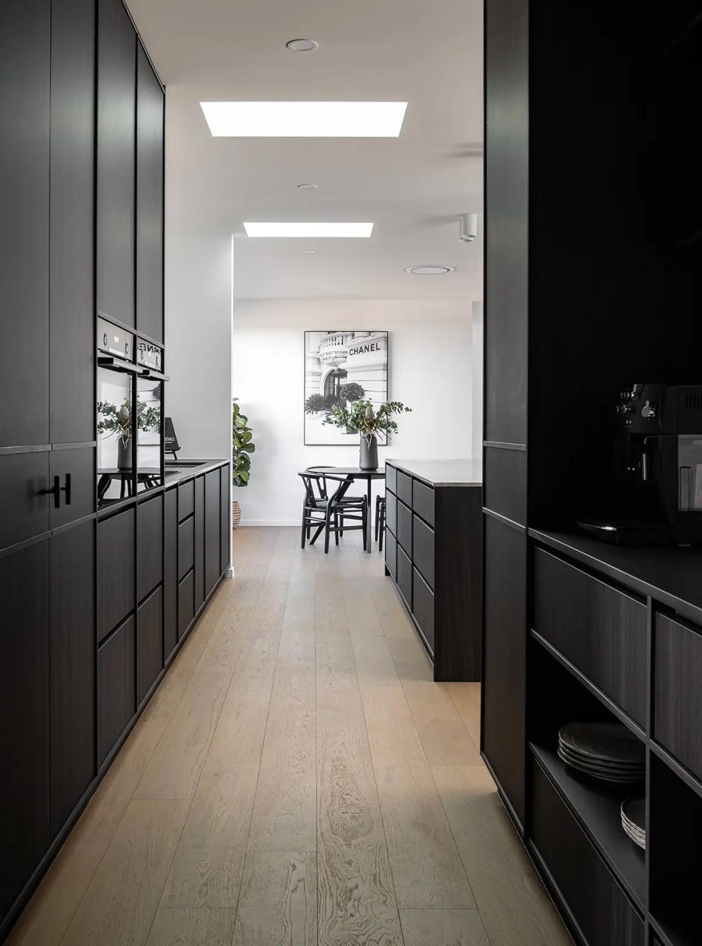 Project Ward 2.0 (Sleek kitchen with black cabinetry, light wood flooring, skylights, and a modern dining area in view)