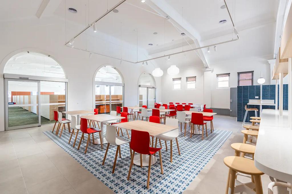 Downlands College Toowoomba Refurbishment (Bright dining space with wood tables, red and white chairs, blue patterned floor tiles, and arched doorways.)
