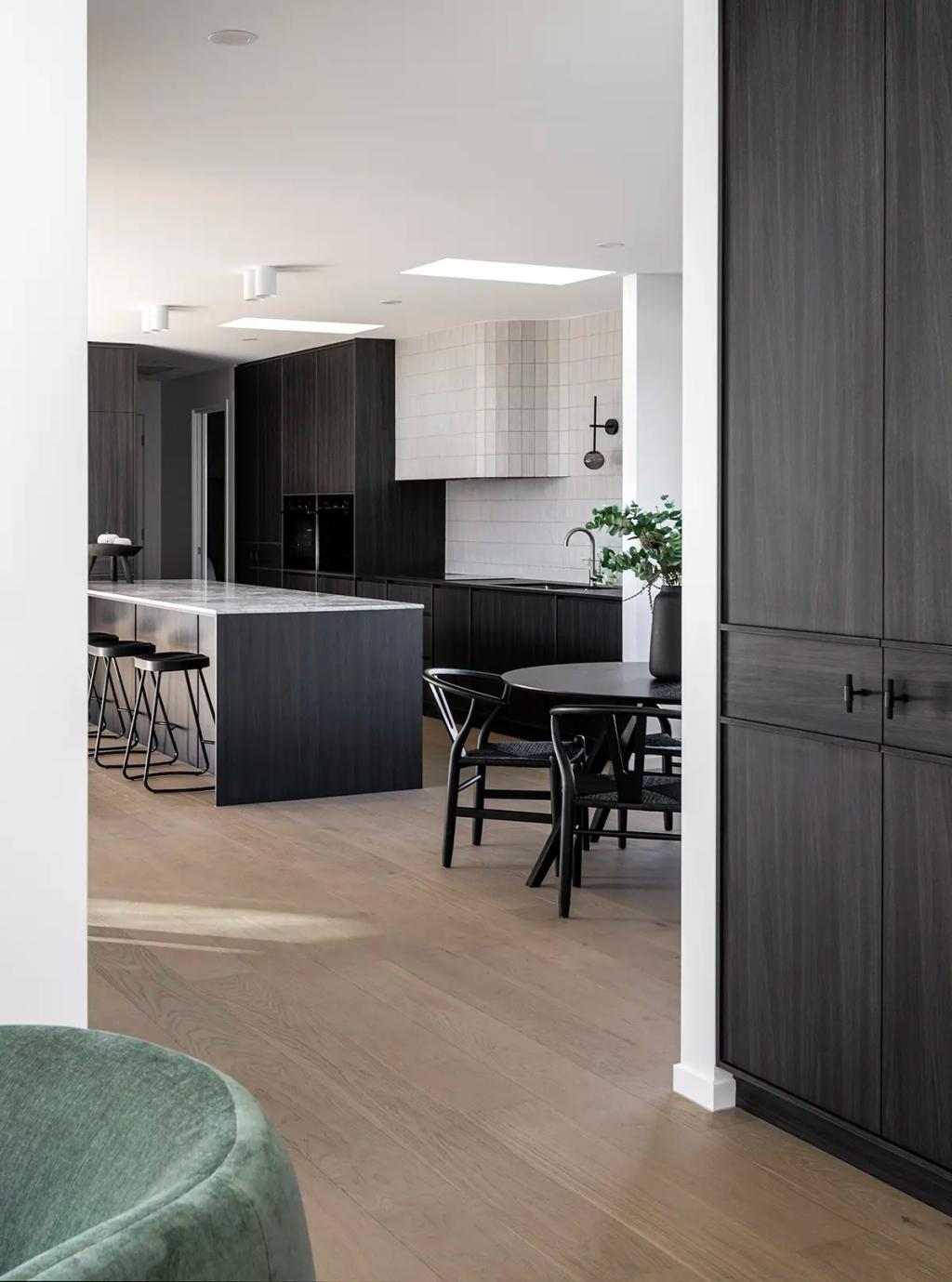 Project Ward 2.0 (A modern kitchen with dark cabinetry, a sleek marble island, black chairs around a dining table, and light wood flooring)