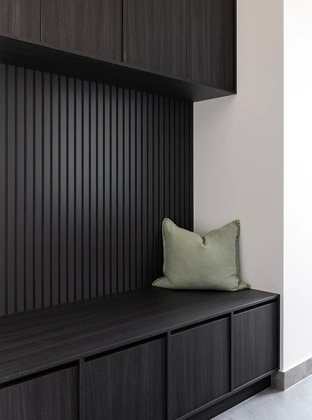 Project Ward 2.0 (A modern mudroom with dark wood cabinetry, a black slatted wall, and a soft green cushion on the bench)