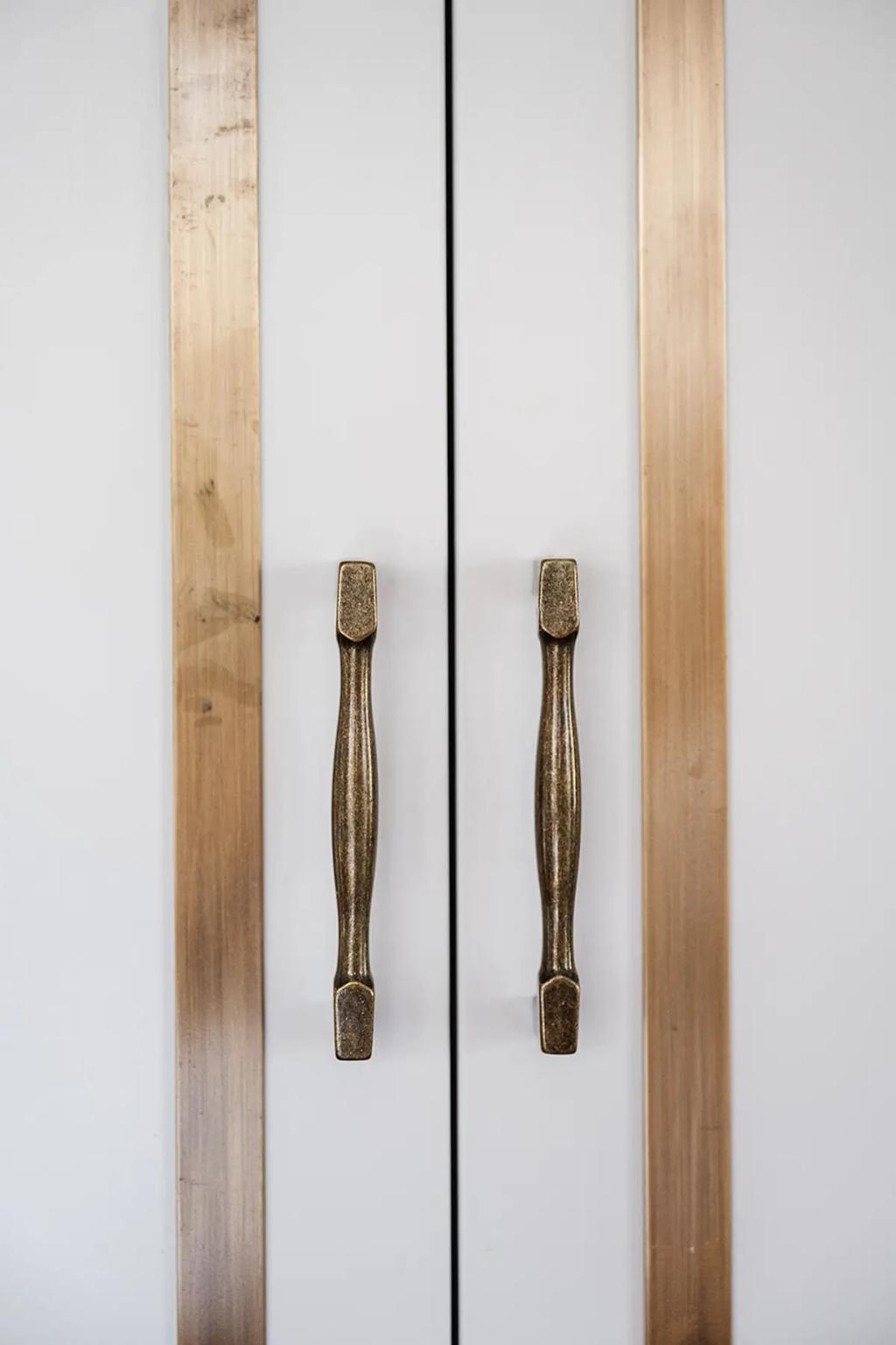 Project Coral Sea (Close-up of white cabinet doors with brass trim and antique-style brass handles in a modern kitchen)