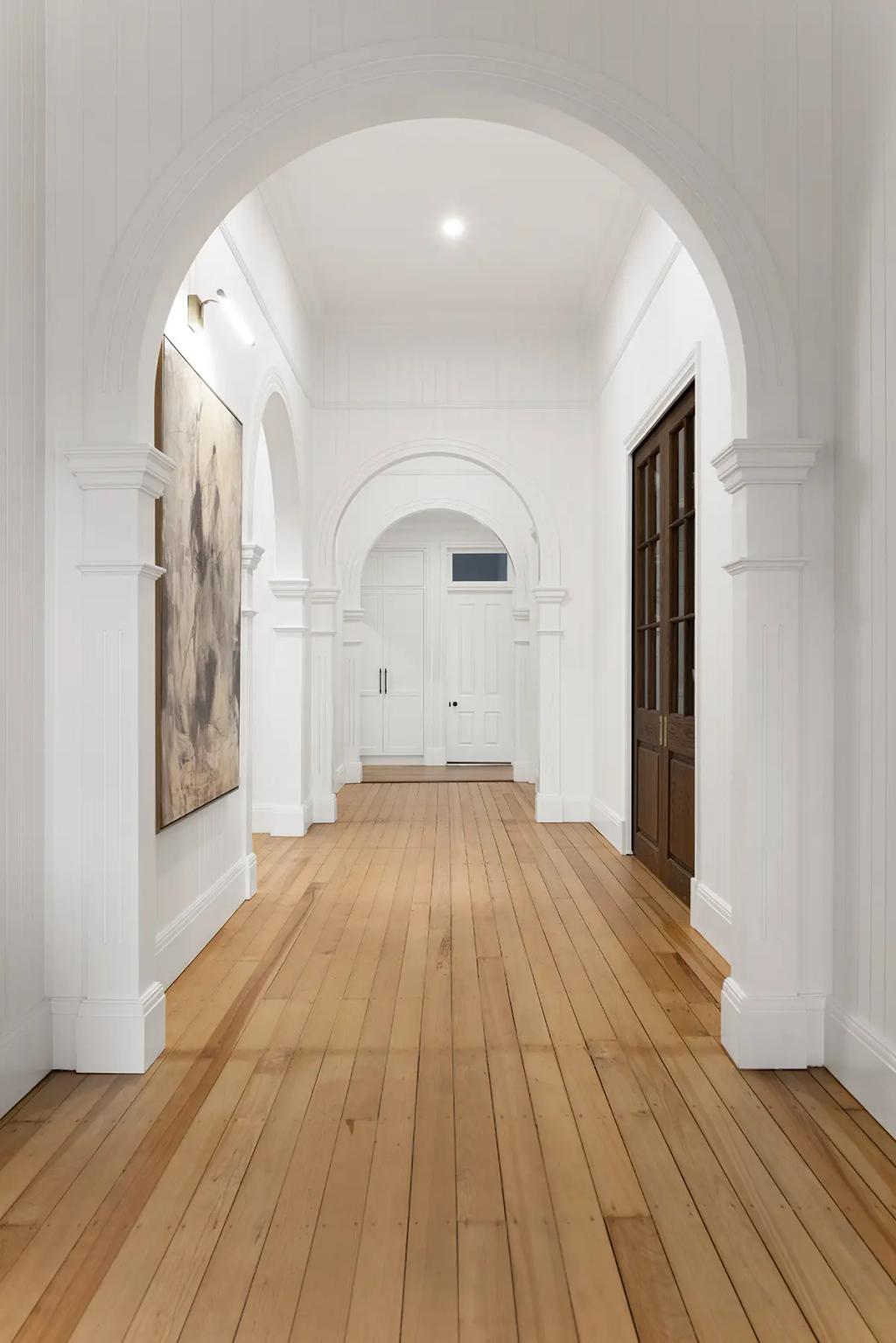 Project Franklin (Elegant hallway with natural wood flooring and classic white archways leading to a closed door.)