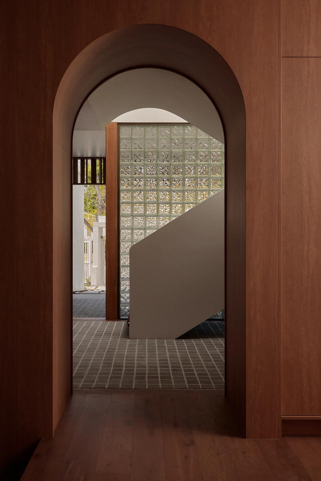 Project Riverton (View through a wood-framed arched doorway to a staircase with a glass block wall.)