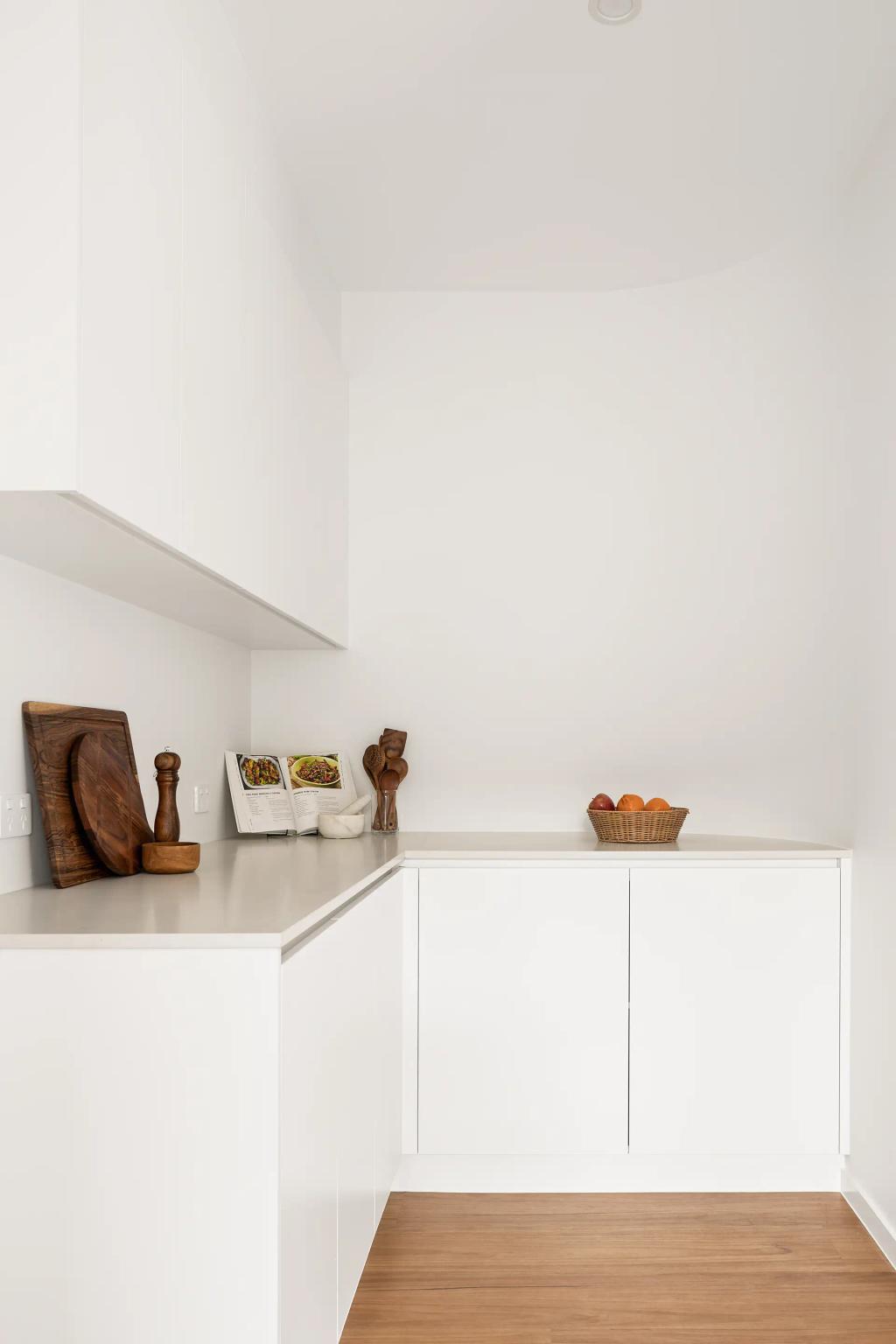 Project Ward (Minimalist white kitchen nook with wooden cutting boards, utensils, a cookbook, and a fruit basket)