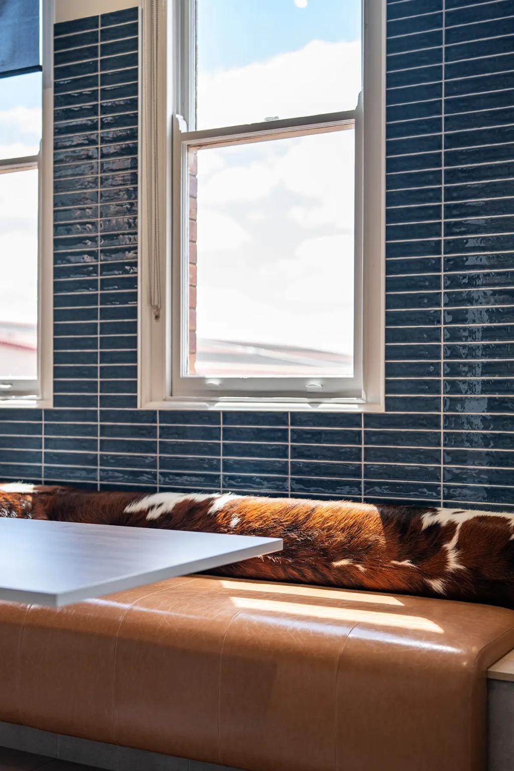 Downlands College Toowoomba Refurbishment (Close-up of a window-side booth with brown leather seating, cowhide cushion, and glossy blue tile wall.)