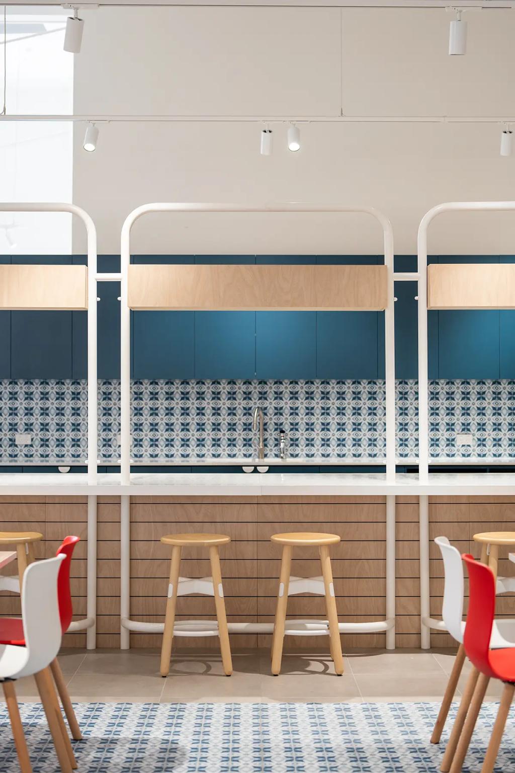 Downlands College Toowoomba Refurbishment (Colorful kitchen space with patterned blue backsplash, wood paneling, bar stools, and red-accented chairs.)