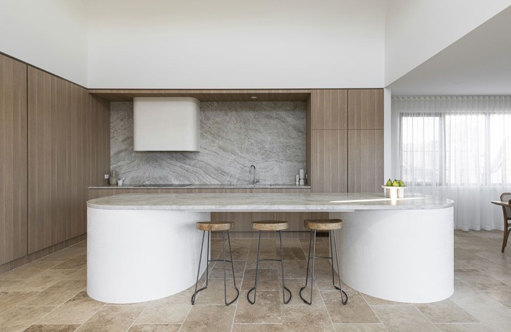 Palmera (Curved white island with stone benchtop, timber cabinetry and grey stone splashback)