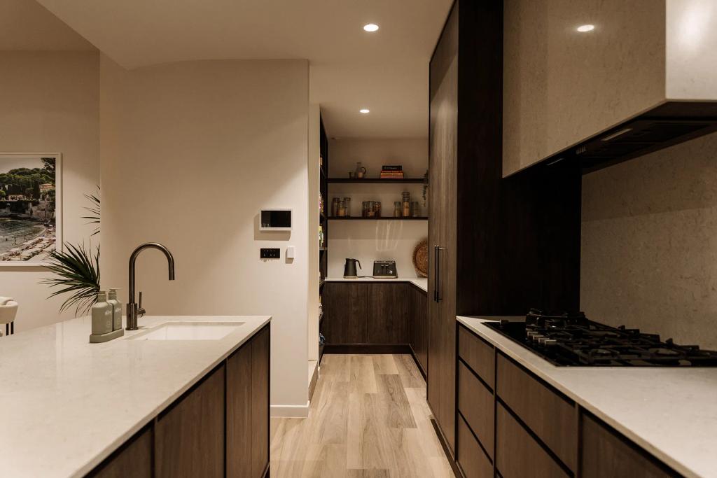Lavish Morada (Modern kitchen with dark cabinetry, gas stove, island sink, and walk-in pantry with shelving.)