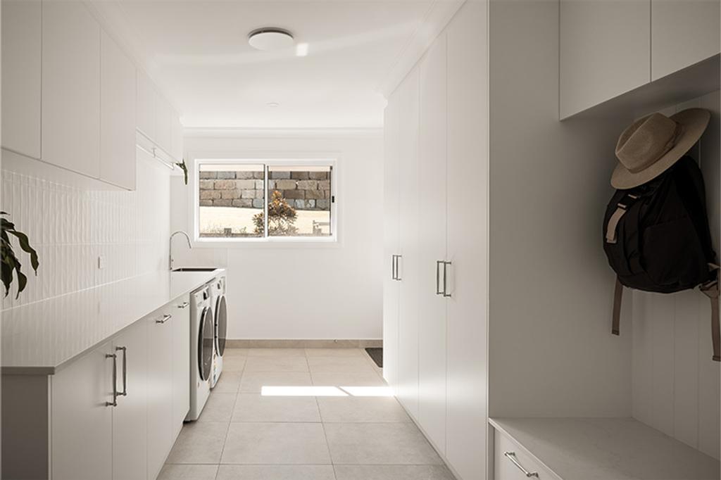 A long row of white cabinets and countertops along one wall, with a washing machine and dryer visible.