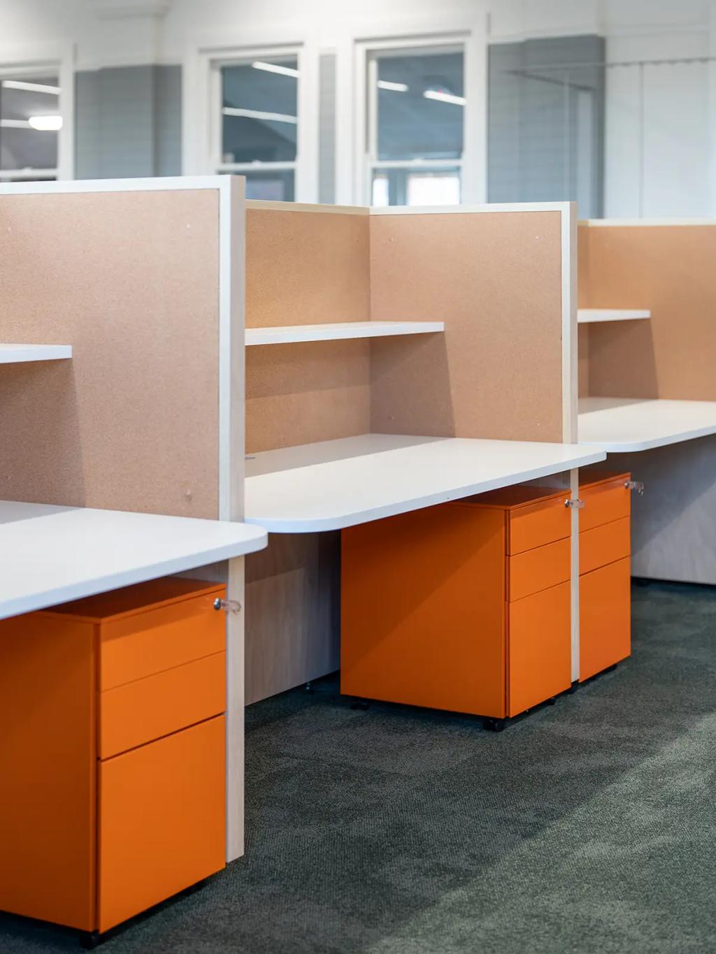 Downlands College Toowoomba Refurbishment (Office cubicles with white desktops, corkboard partitions, and bright orange mobile pedestal drawers.)