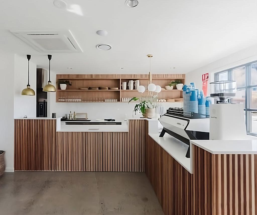 Minimalist cafe counter with vertical wood slats, white countertop, and espresso machine.