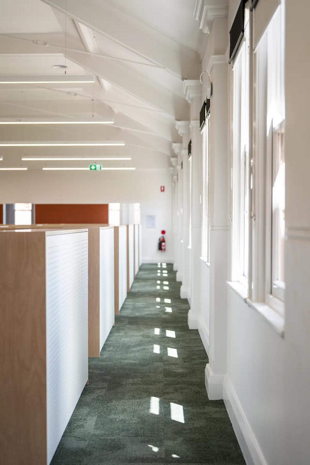 Downlands College Toowoomba Refurbishment (Sunlit office hallway with green carpet, white-framed windows, and rows of modern workstations on the left.)